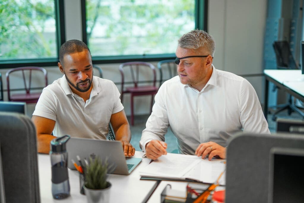 Two employees sitting next to each other at a desk, talking.