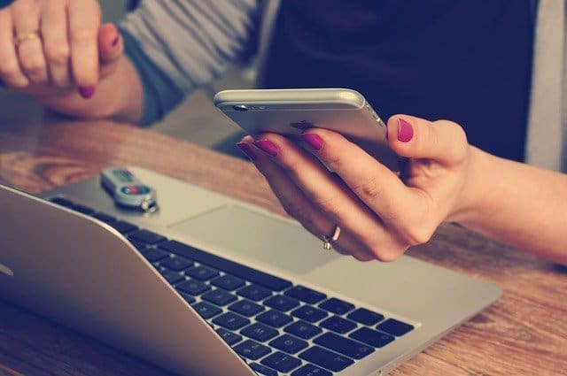 A laptop and a woman's hands holding a mobile phone