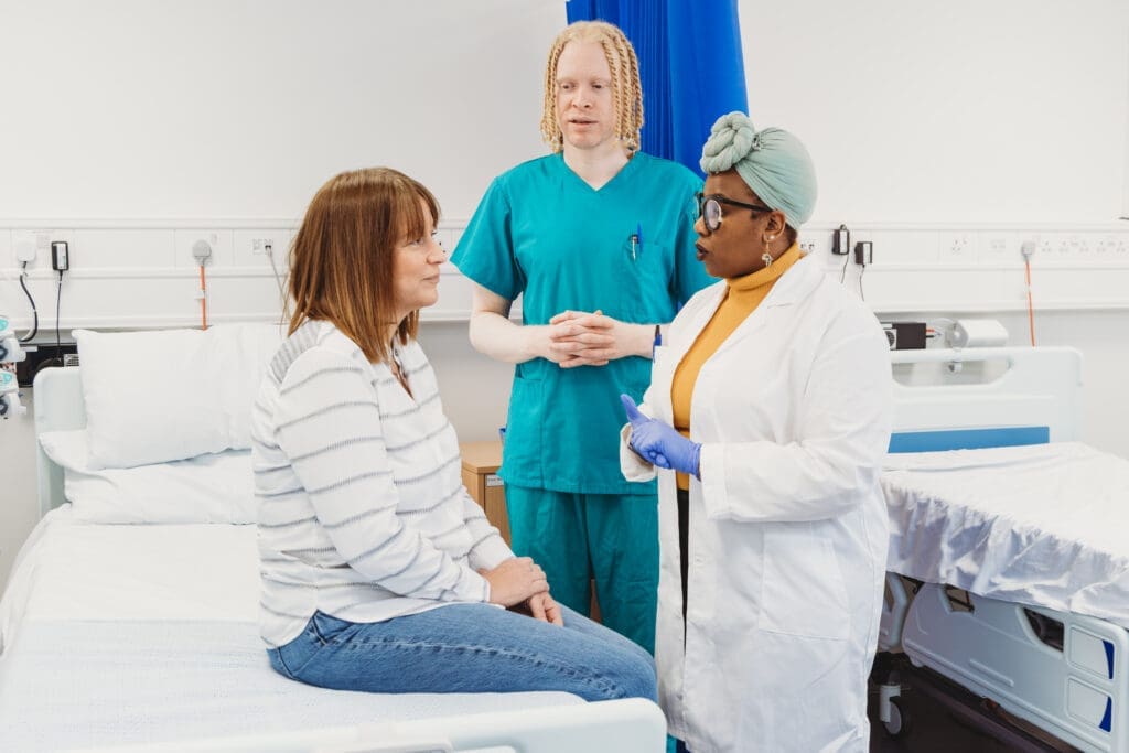 A patient with a mental health condition speaks to two doctors. Left: A man with albinism and sight loss and right a woman with multiple disabilities (Long Covid, Fatigue, Brain fog)