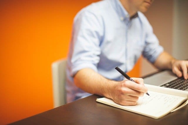 An employee sitting at a desk, making a note with a pen and a notepad.