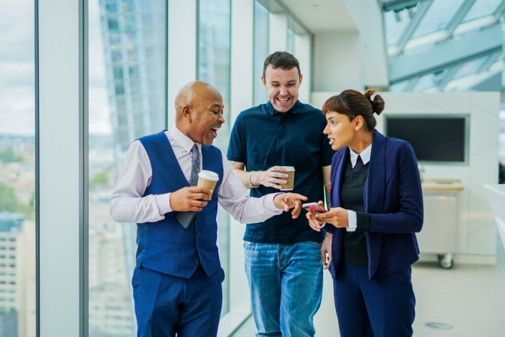 Colleagues with less-visible disabilities walk together smiling with coffees in office