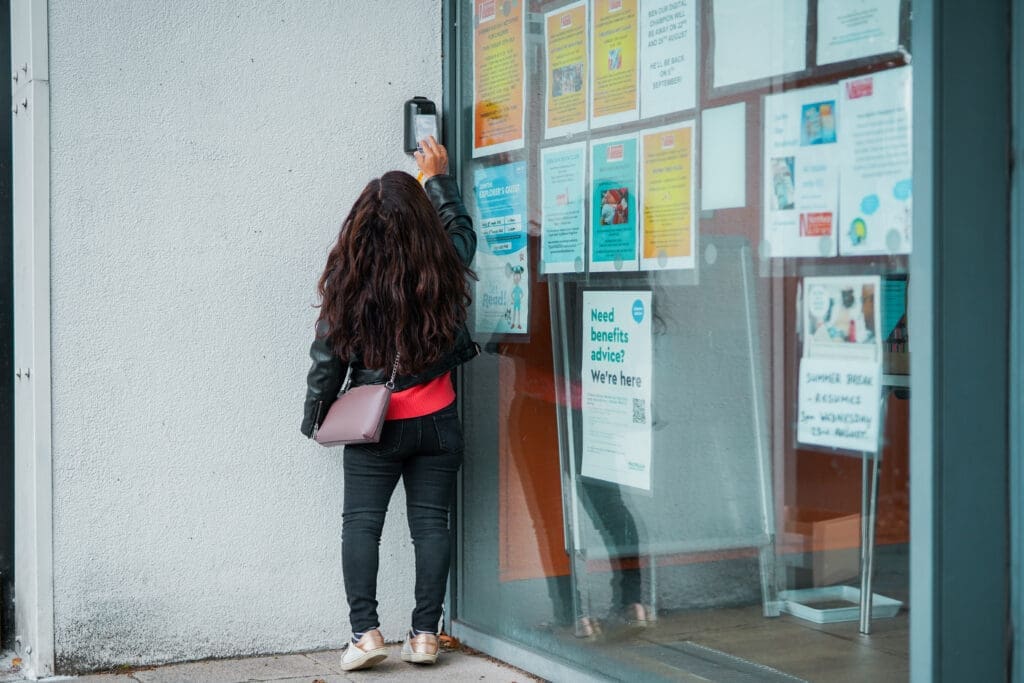 Person who is short in stature reaching to use a card key to enter a library.