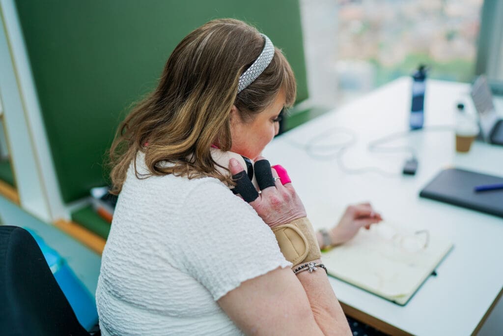 Electric wheelchair user in an office wears a wrist support and writes in a notebook