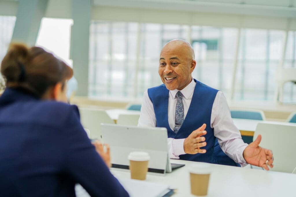 Person with less-visible disability with laptop interacts with colleague at work meeting with coffee
