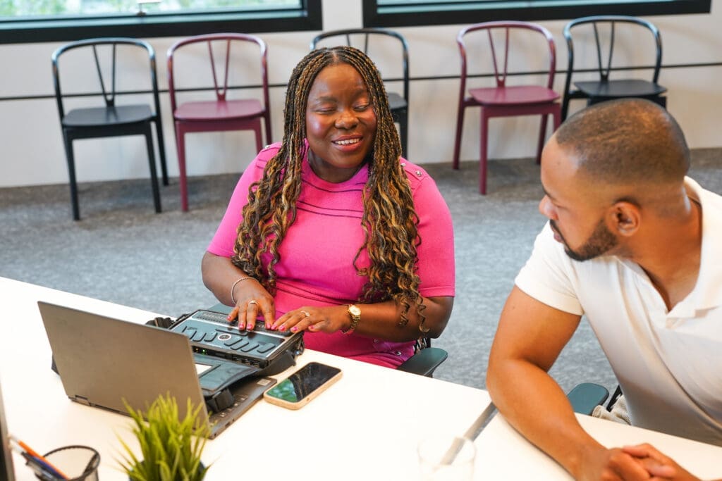 A blind person works on a braille note next to a colleague
