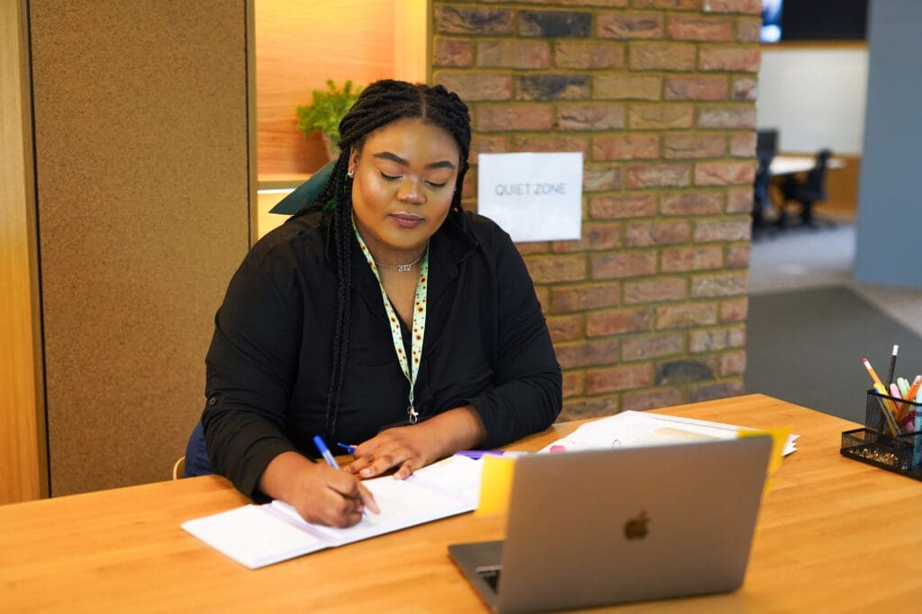 Person wearing a sunflower lanyard to show less-visible disabilities sits and works in quiet zone of office with laptop and notebook