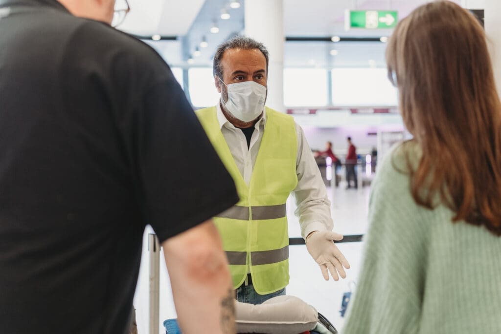 Person wearing a high-vis with less-visible disabilities speaks to two travellers