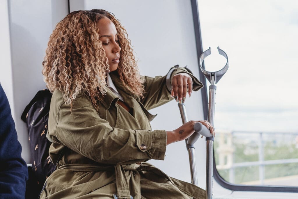 Person sits on public transport while holding their crutches