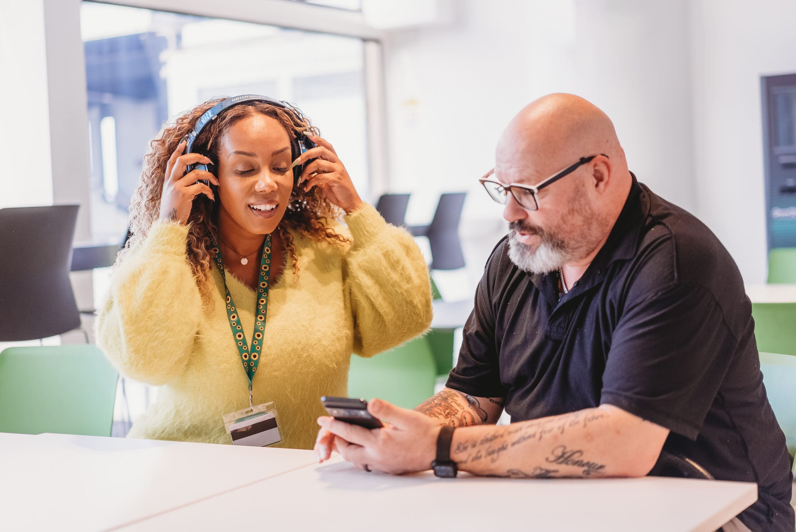 Person wearing a sunflower lanyard uses headphones to listen to audio on phone with colleague.