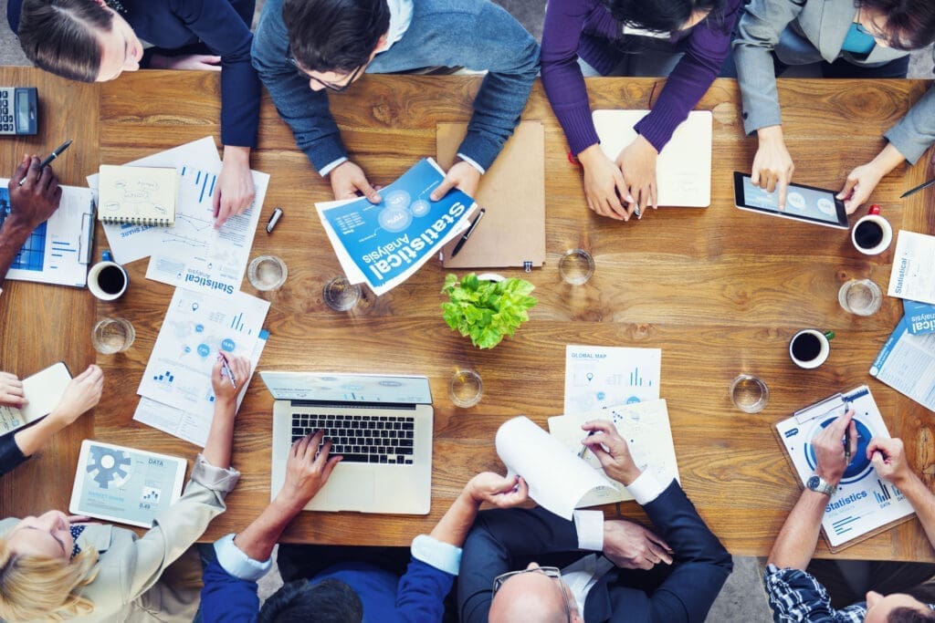 Aerial shot of people in a meeting with laptops, tablets and notepads.