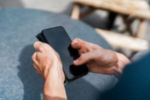 A close up of a man's hands texting on a phone. The man has manual dexterity issues.