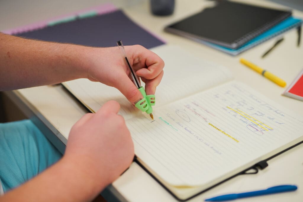 Person with a less-visible disability writes in a notepad using an assistive pen