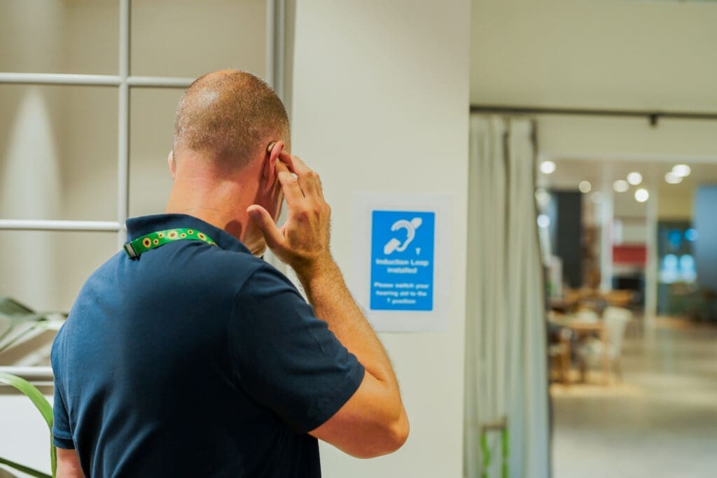 A Deaf person adjusts hearing aid by Induction Loop Installed notice on wall