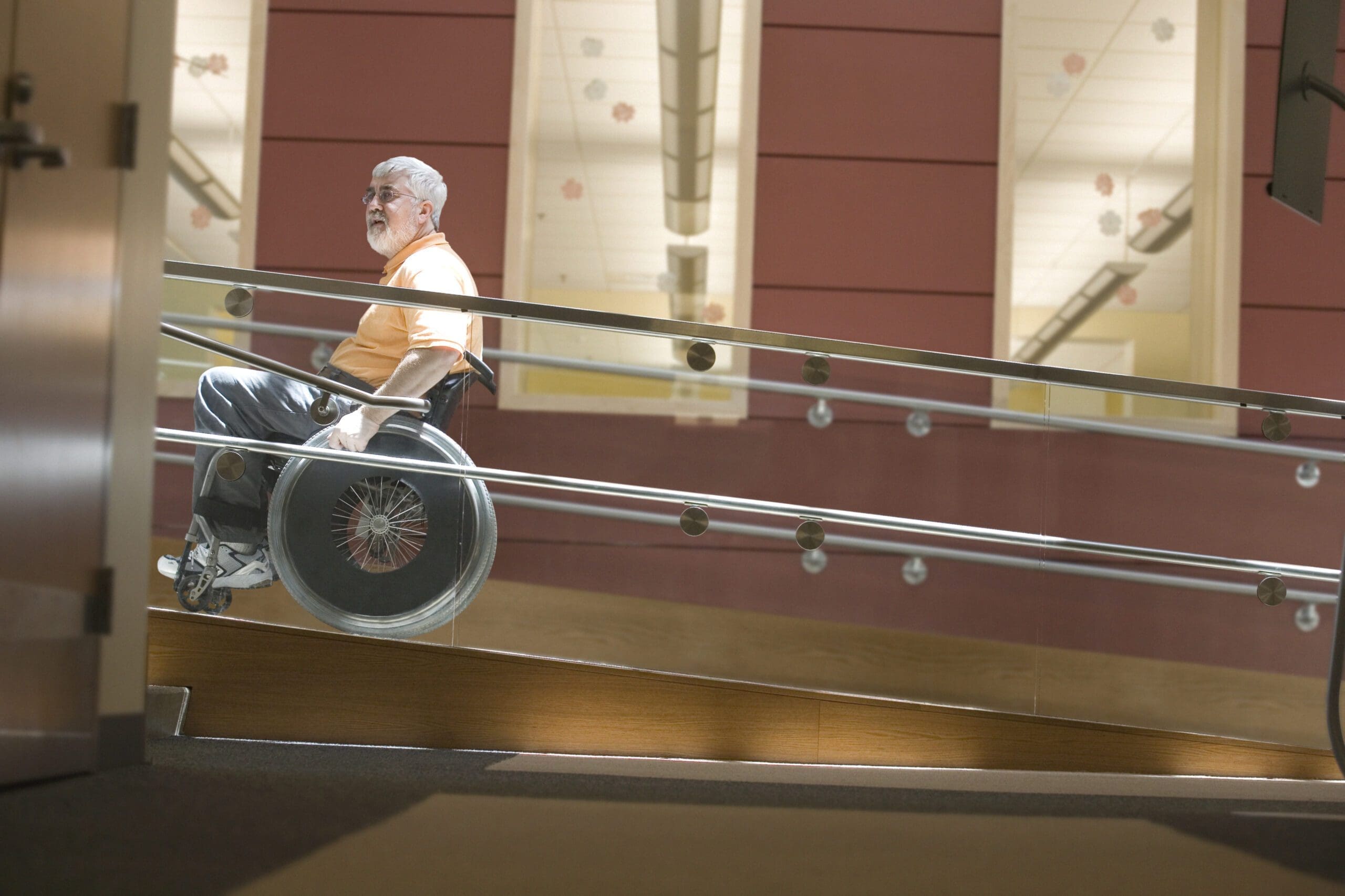 Side profile of a mature man sitting in a wheelchair on a wheelchair ramp
