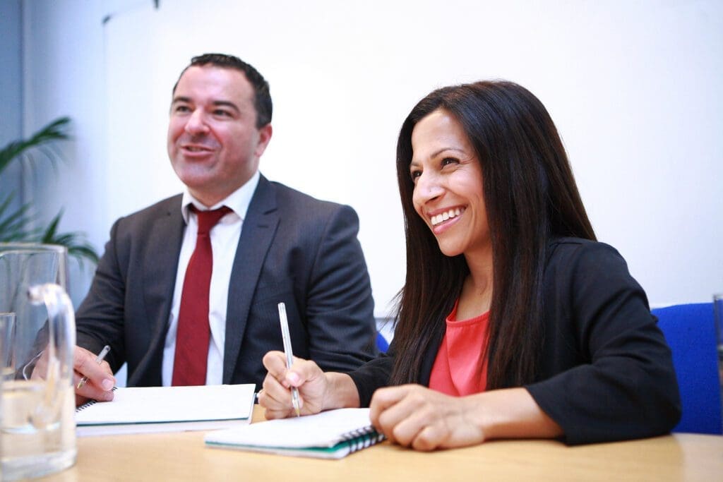 A man and a woman in a meeting, smiling at someone off camera