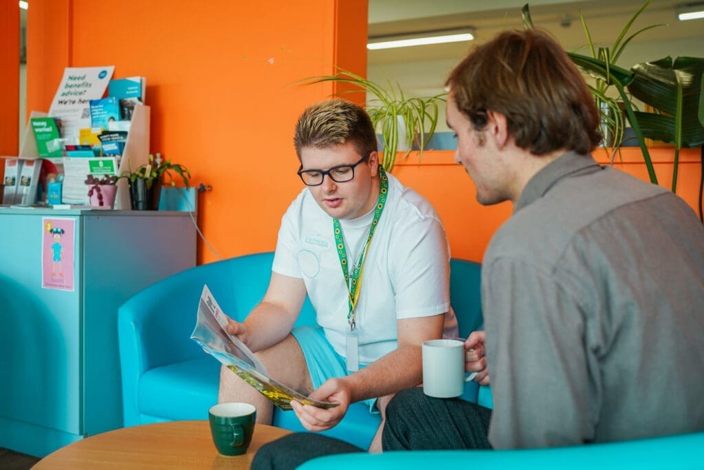 View all results Person with less-visible disability shows friend a leaflet in a library.