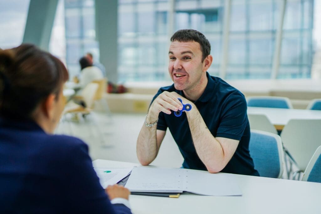 Person with less-visible disabilities uses a fidget spinner whilst having a meeting with a colleague