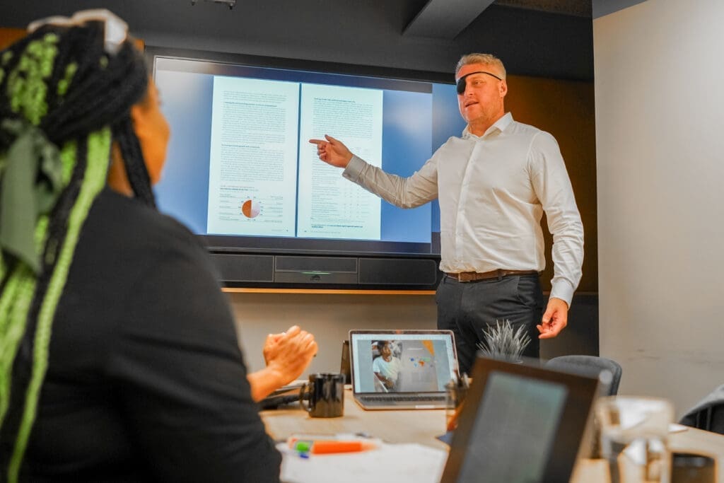 Person with facial difference and sight loss presents to colleague in meeting room.