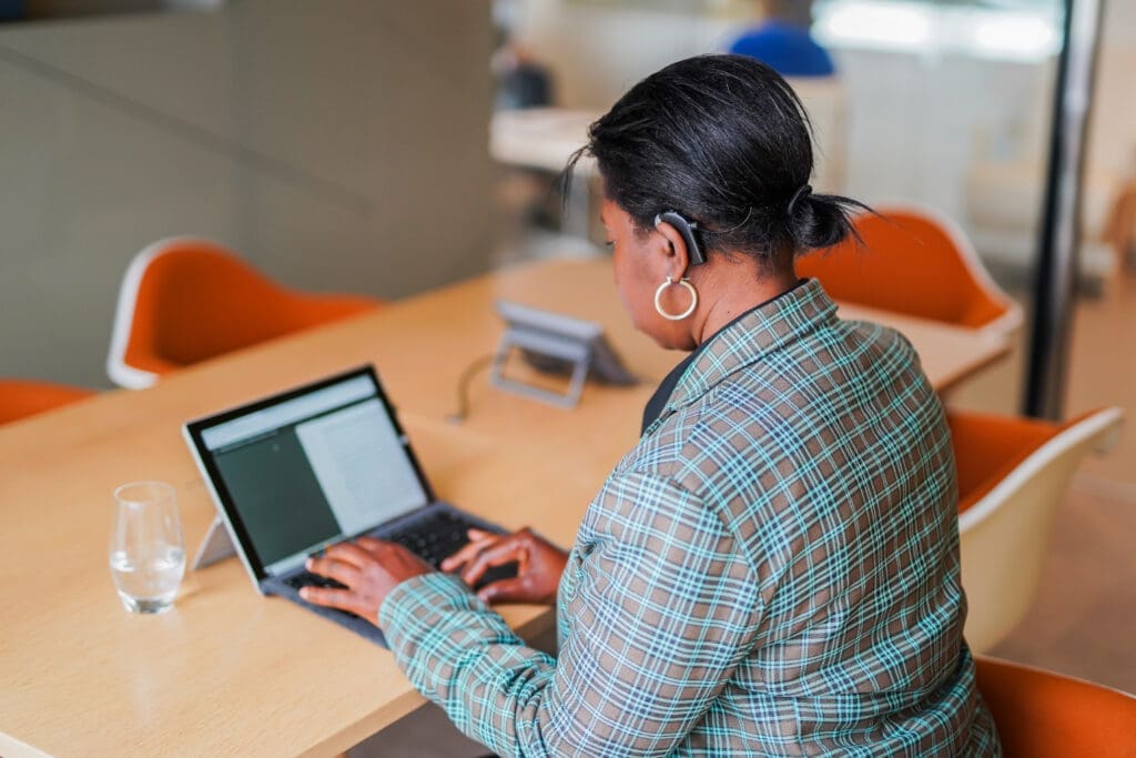Deaf person wearing hearing aid works alone at laptop in meeting room