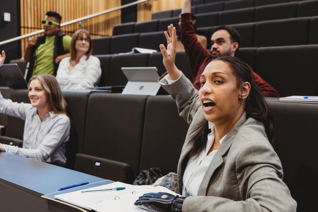 Person with bionic arm and other audience members with less-visible disabilities raise their hands at an event