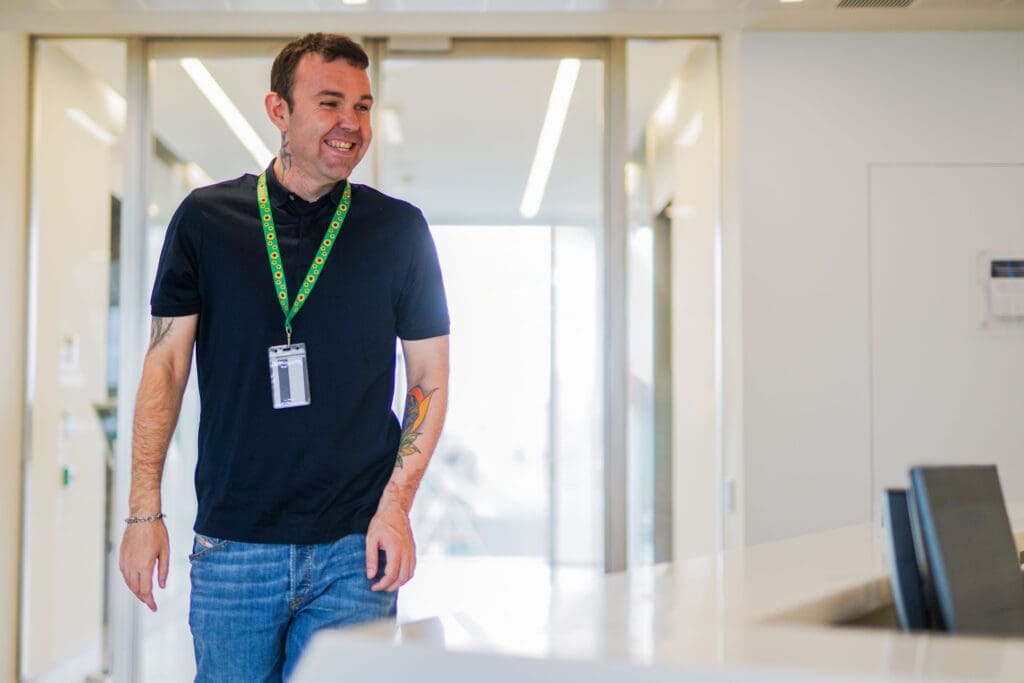 A person with a less-visible disability (learning disabilities) smiles and walks down corridor past desk