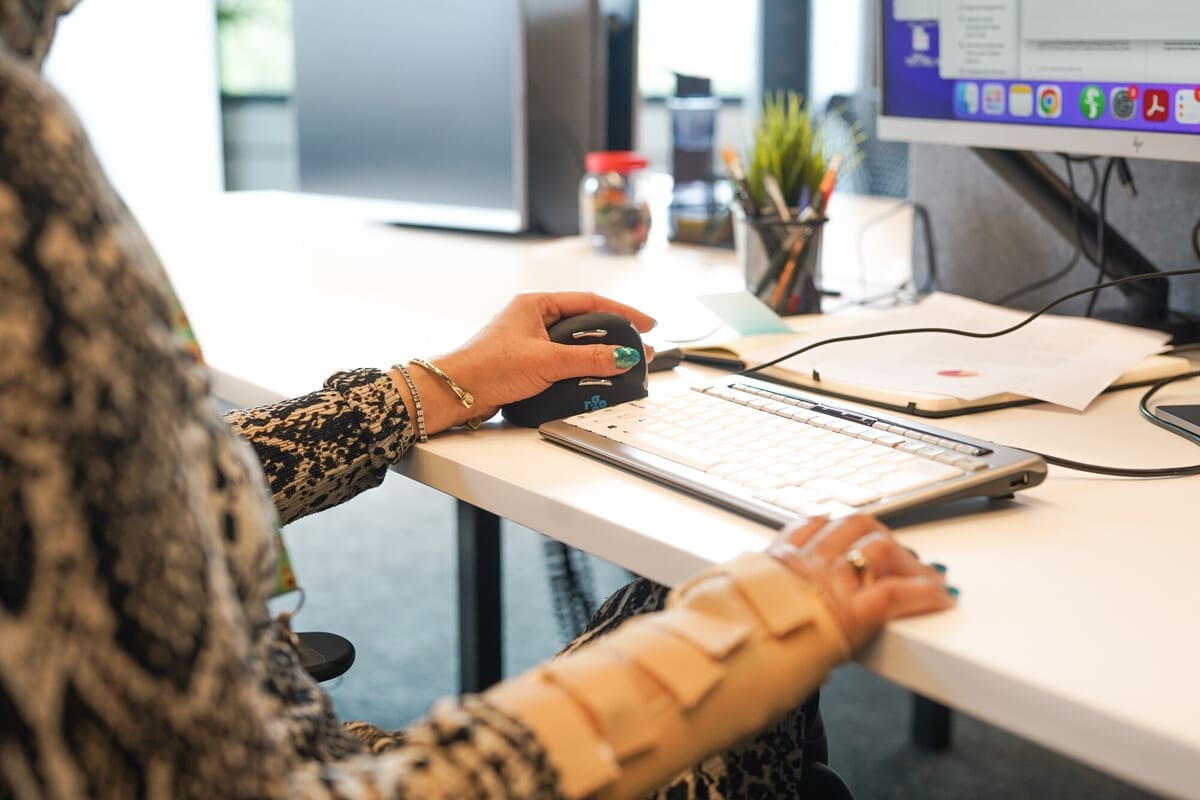Person works at desk with ergonomic mouse wearing wrist support Close up on a professional's hands as they work at a desk using an ergonomic mouse. They are wearing a wrist support.