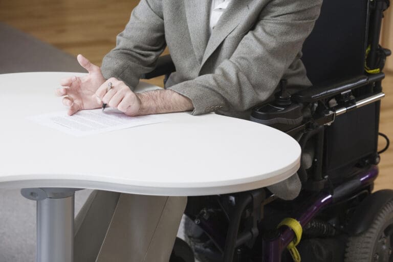 A wheelchair user signs a document.