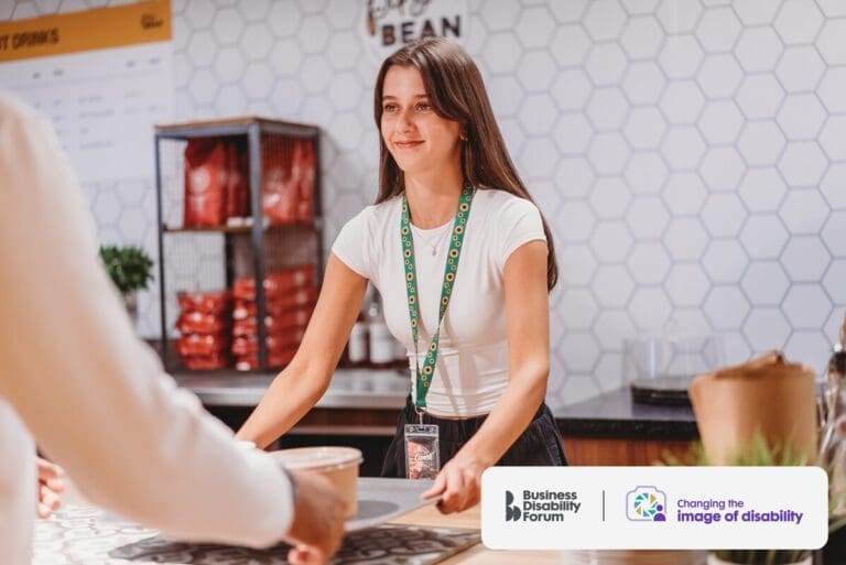 Young white server wearing a lanyard to show she has a less-visible disability hands a tray to a customer.