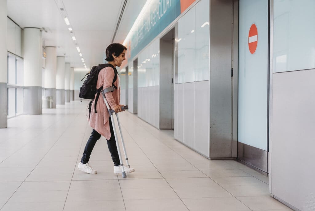 Person who is short in stature uses crutches and walks towards a door.