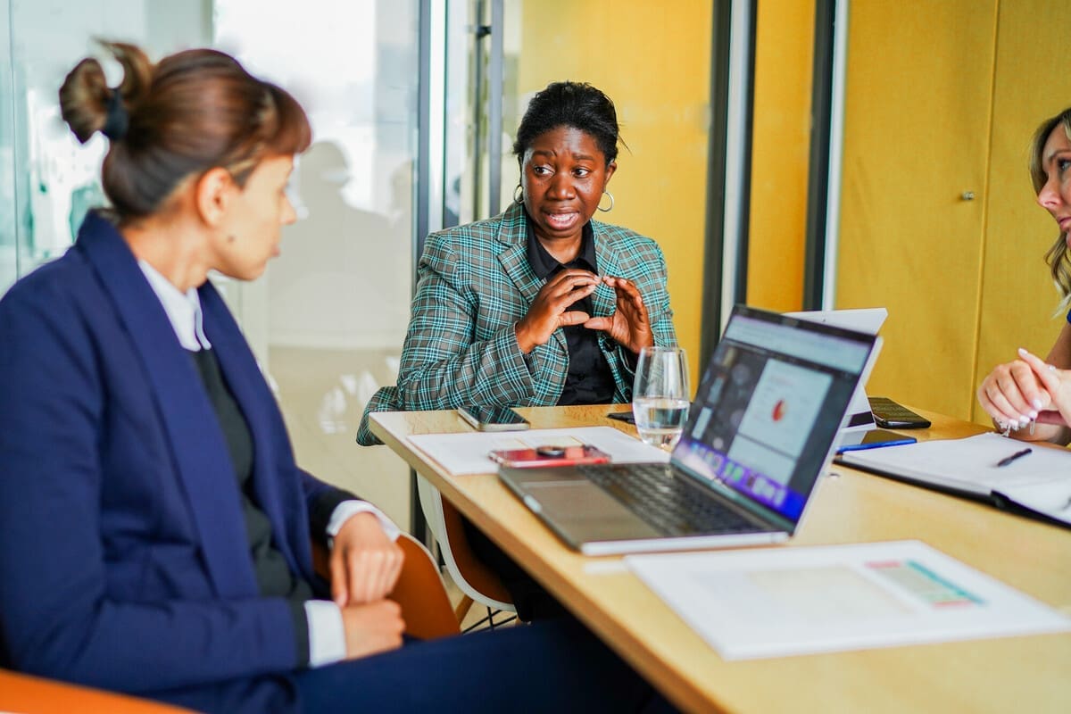 Three colleagues with diverse disabilities at a large table in a meeting room. One is using sign language.