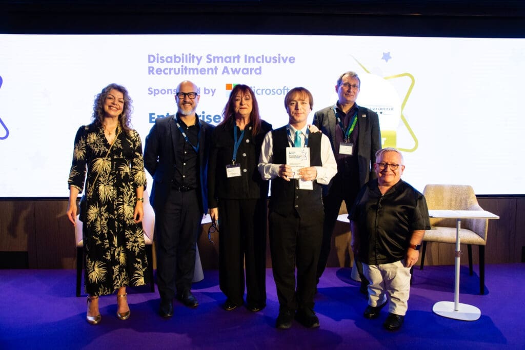 The Enterprise East CIC team posing on stage with the ceremony hosts and their category's sponsors after winning the Inclusive Recruitment Award at the Disability Smart Awards 2025.