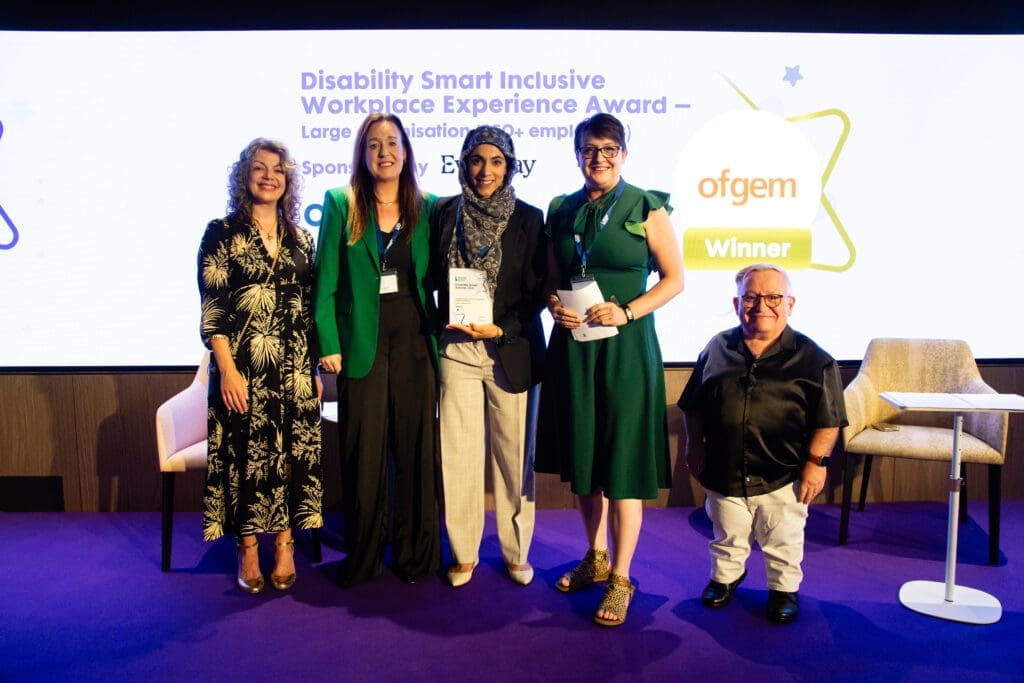 The Ofgem team posing on stage with ceremony hosts Diane Lightfoot (left) and Simon Minty (right) after winning the Inclusive Workplace Experience Award (large organisation) at the Disability Smart Awards 2025.