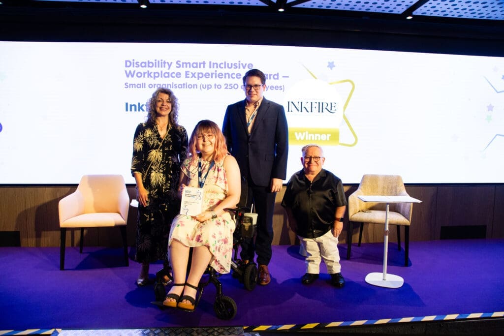 The Inkfire team posing on stage with ceremony hosts Diane Lightfoot (left) and Simon Minty (right) after winning the Inclusive Workplace Experience Award (small organisation) at the Disability Smart Awards 2025.