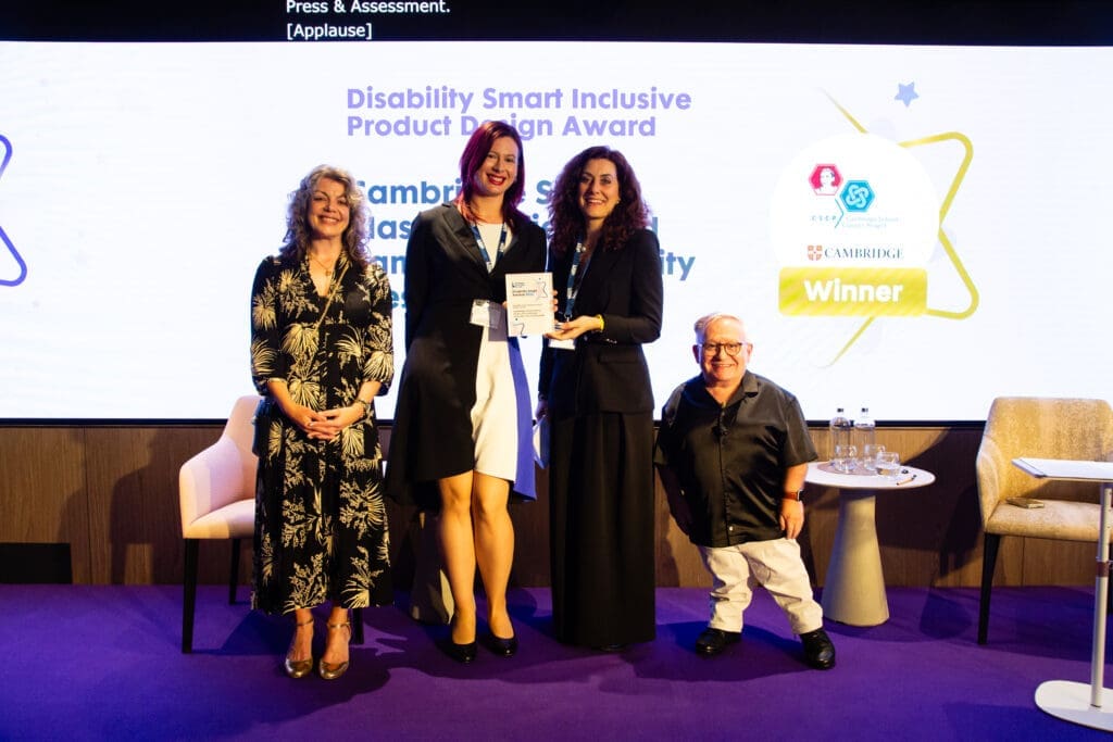 The Cambridge School Classics Project and Cambridge University Press & Assessment team posing on stage with ceremony hosts Diane Lightfoot (left) and Simon Minty (right) after winning the Inclusive Product Design Award at the Disability Smart Awards 2025.