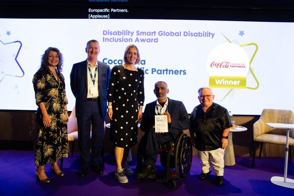 The Coca-Cola Pacific Partners team posing on stage with ceremony hosts Diane Lightfoot (left) and Simon Minty (right) after winning the Global Disability Inclusion Award at the Disability Smart Awards 2025.