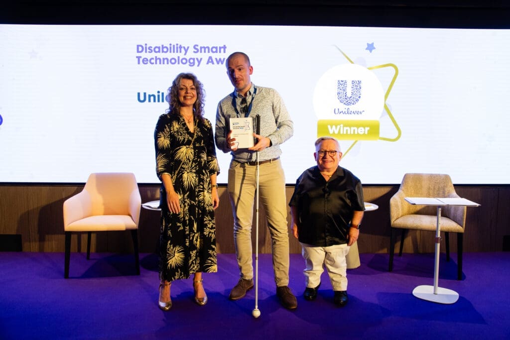 The Unilever team posing on stage with ceremony hosts Diane Lightfoot (left) and Simon Minty (right) after winning the Technology Award at the Disability Smart Awards 2025.