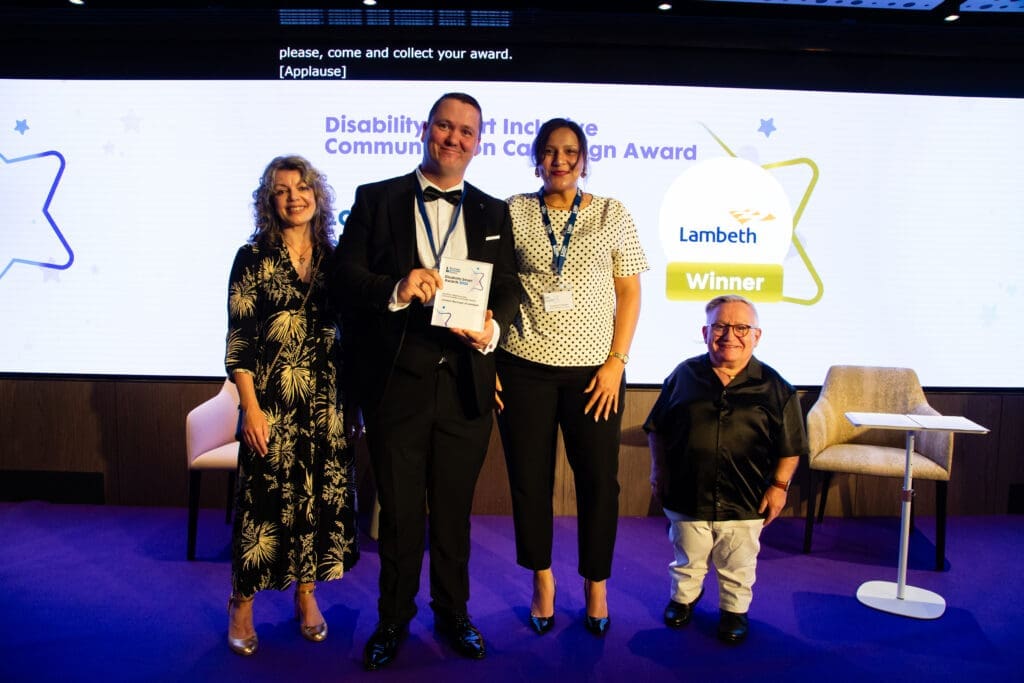 The Borough of Lambeth team posing on stage with ceremony hosts Diane Lightfoot (left) and Simon Minty (right) after winning the Inclusive Communication Campaign Award at the Disability Smart Awards 2025.