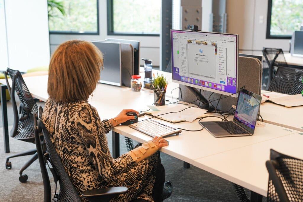 Professional with less-visible disabilities, who wears a wrist support, working at a desk using an ergonomic mouse and accessible keyboard.