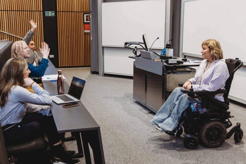 Lecturer using a mechanical wheelchair gives a presentation to students.