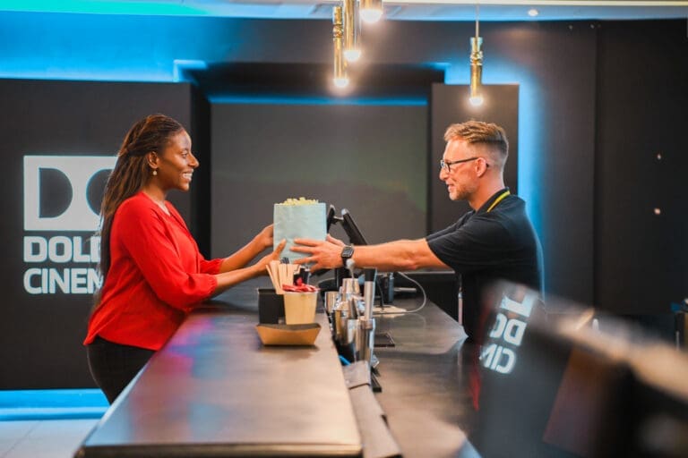 Sales assistant with less-visible disability passes popcorn to customer at cinema