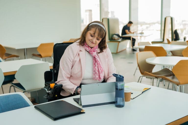 A wheelchair user with Chanarin Dorfman Sydnrome working from a laptop at an office desk
