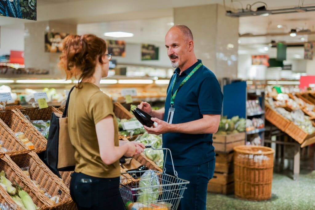 A Deaf sales assistant helps a customer who has a less-visible disability (PMDD) in a supermarket