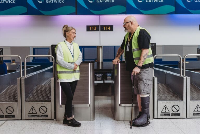 An airport worker who wears a medical boot and uses a walking stick talks to a colleague with less-visible disabilities