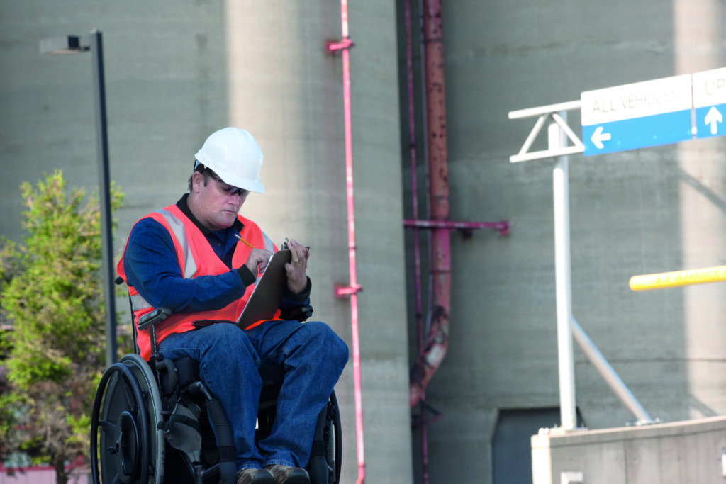 A wheelchair user at a construction site writing on a clipboard