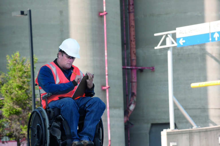 A wheelchair user at a construction site writing on a clipboard