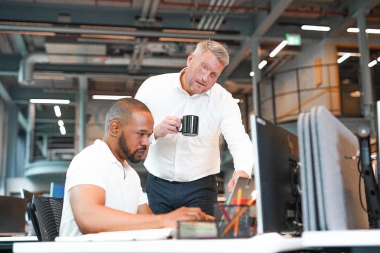 Man with facial difference looks at computer screen with colleague in office