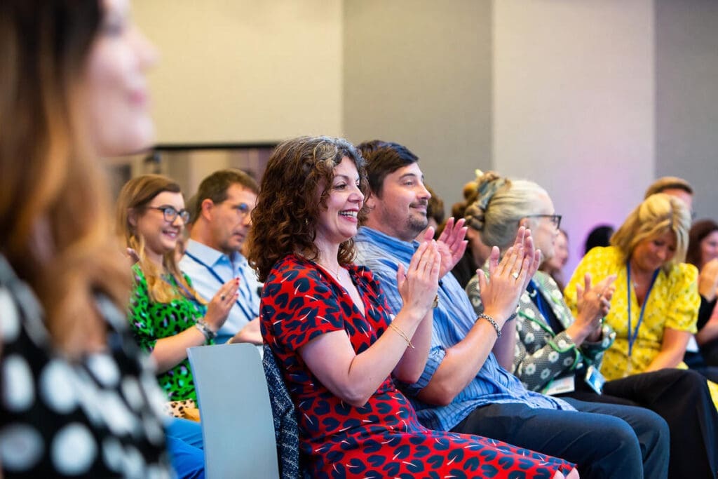 Smiling audience members clapping at an event.