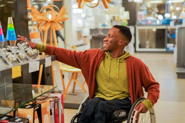 A ​male ​wheelchair ​user ​with ​Spina ​Bifida ​reaches ​for ​a ​lava ​lamp ​in ​a ​retail ​store