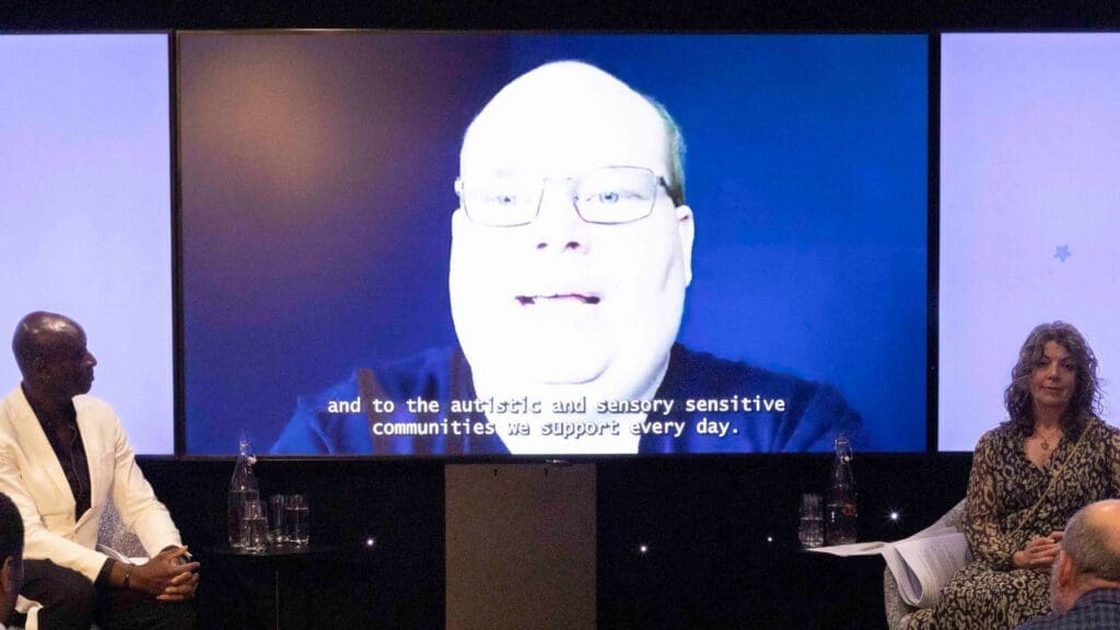 Speakers on stage watching a video message displayed on a large screen during the Disability Smart Impact Awards 2026.
