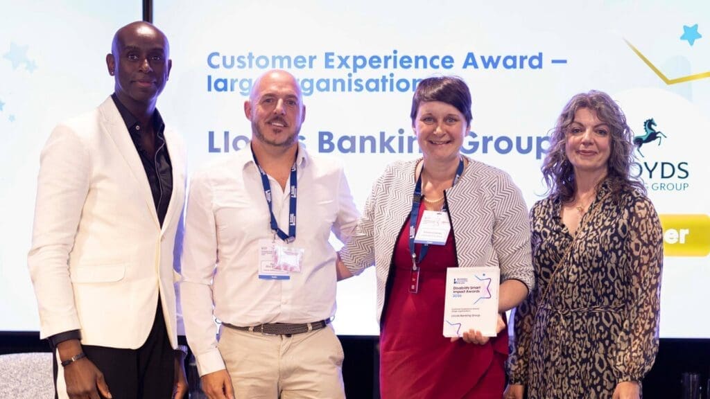 Lloyds Banking Group team receiving the Customer Experience Award on stage with presenters at the Disability Smart Impact Awards 2026.